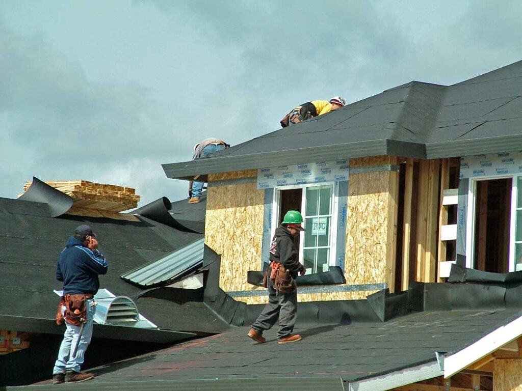 Homeowner reviewing roof shingles and attic moisture signs with an inspector beside a house.