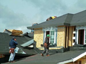Homeowner reviewing roof shingles and attic moisture signs with an inspector beside a house.