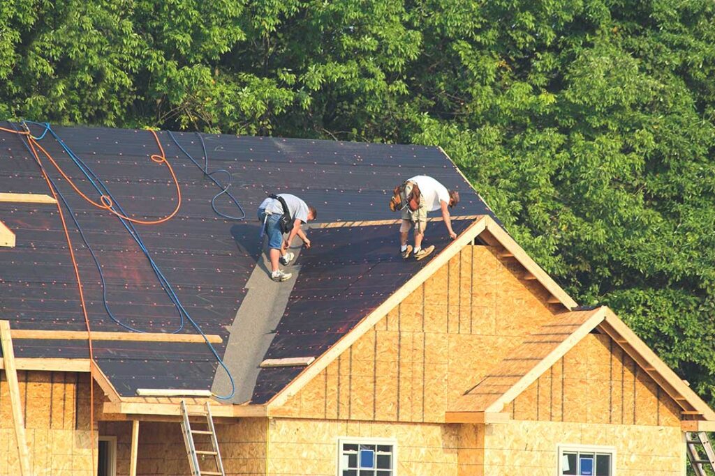Person using a garden hose from the ground to gently rinse debris from a residential shingle roof.