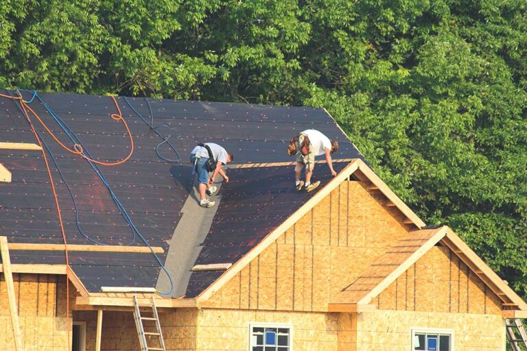 Person using a garden hose from the ground to gently rinse debris from a residential shingle roof.