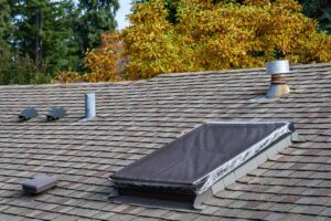 Person safely inspecting roof shingles and gutters beside a two-story home in autumn